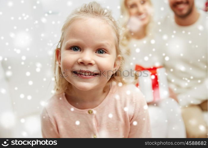 family, christmas, holidays and people concept - happy mother, father and little daughter with gift box sitting on sofa at home