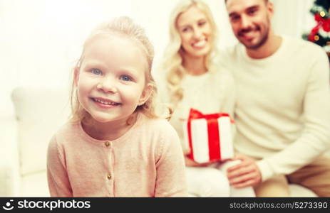 family, christmas, holidays and people concept - happy mother, father and little daughter with gift box sitting on sofa at home. happy family at home with christmas gift box