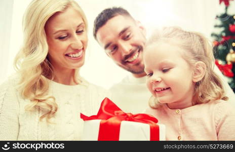 family, christmas, holidays and people concept - happy mother, father and little daughter with gift box sitting on sofa at home. happy family at home with christmas gift box