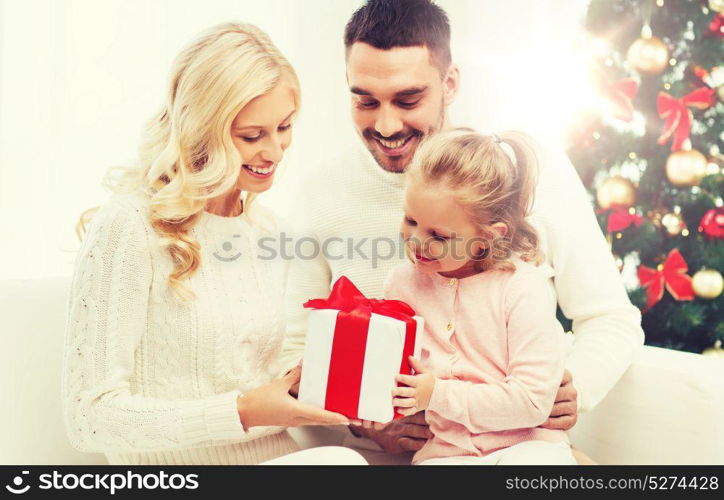 family, christmas, holidays and people concept - happy mother, father and little daughter with gift box sitting on sofa at home. happy family at home with christmas gift box