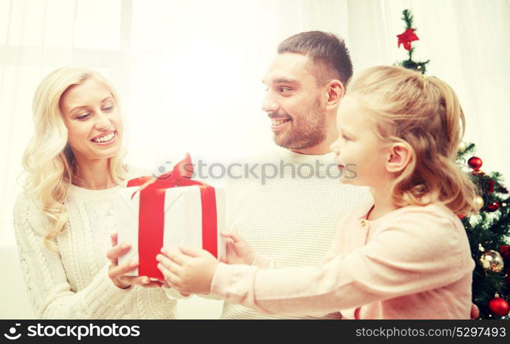family, christmas, holidays and people concept - happy mother, father and little daughter with gift box sitting on sofa at home. happy family at home with christmas gift box