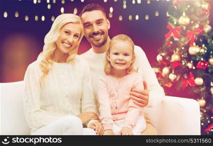 family, christmas, holidays and people concept - happy mother, father and little daughter sitting on sofa over lights background. happy family over christmas tree