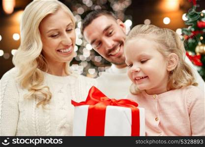 family, christmas, holidays and people concept - happy mother, father and little daughter with gift box over lights background. happy family at home with christmas gift box