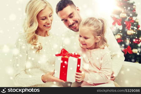 family, christmas, holidays and people concept - happy mother, father and little daughter with gift box sitting on sofa at home. happy family at home with christmas gift box