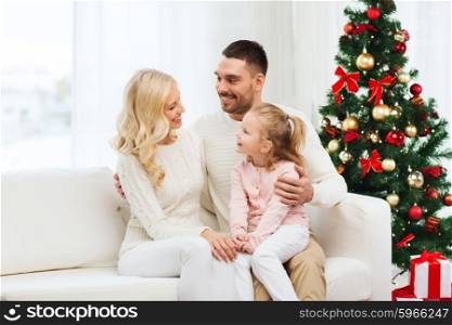 family, christmas, holidays and people concept - happy mother, father and little daughter sitting on sofa at home