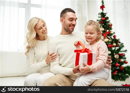 family, christmas, holidays and people concept - happy mother, father and little daughter with gift box sitting on sofa at home