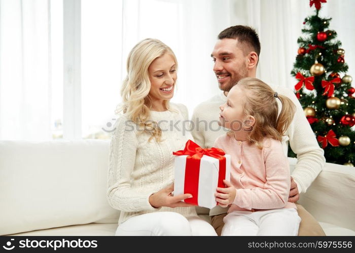 family, christmas, holidays and people concept - happy mother, father and little daughter with gift box sitting on sofa at home