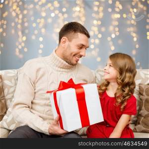 family, christmas, holidays and people concept - smiling father and daughter with gift box looking at each other over lights background