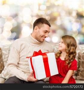 family, christmas, holidays and people concept -smiling father and daughter with gift box over lights background