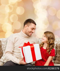 family, christmas, holidays and people concept -smiling father and daughter with gift box over beige lights background