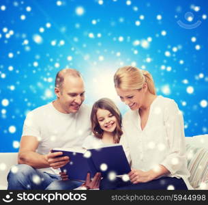 family, christmas, holidays and people - smiling mother, father and little girl reading book over blue snowy background