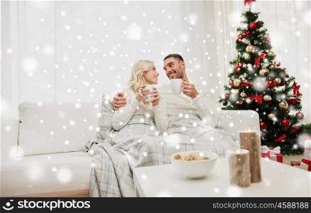 family, christmas, holidays, love and people concept - happy couple covered with plaid drinking tea and sitting on sofa at home