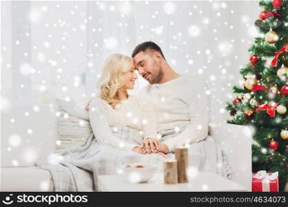 family, christmas, holidays, love and people concept - happy couple covered with plaid sitting on sofa at home