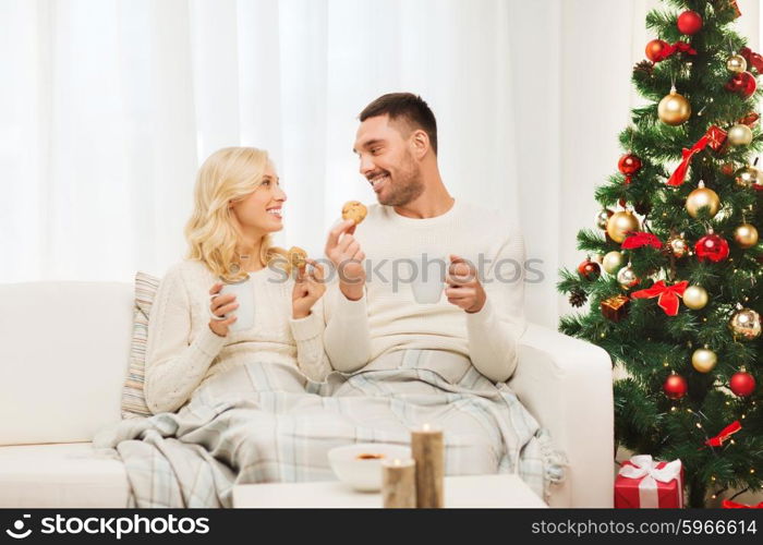 family, christmas, holidays, love and people concept - happy couple covered with plaid drinking tea and sitting on sofa at home