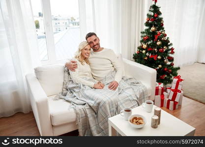 family, christmas, holidays, love and people concept - happy couple covered with plaid sitting on sofa at home