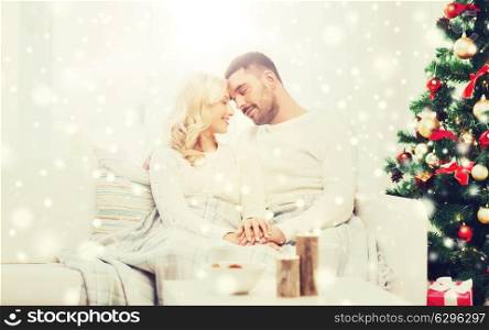 family, christmas, holidays, love and people concept - happy couple covered with plaid sitting on sofa at home. happy couple at home with christmas tree