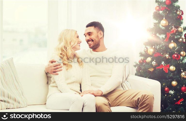 family, christmas, holidays, love and people concept - happy couple sitting on sofa at home. happy couple at home with christmas tree