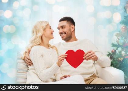 family, christmas, holidays, love and people concept - happy couple with red heart at home over blue lights background