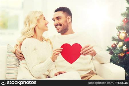 family, christmas, holidays, love and people concept - happy couple with red heart at home. happy couple with red heart at home for christmas