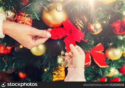 family, christmas, holidays, new year and people concept - close up of mother and child hands decorating christmas tree. close up of family decorating christmas tree