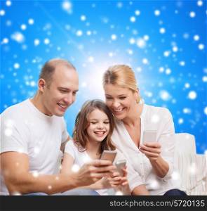 family, christmas holidays, technology and people concept - smiling mother, father and little girl with smartphones over blue snowy background