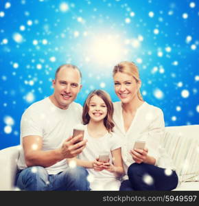 family, christmas holidays, technology and people concept - smiling mother, father and little girl with smartphones over blue snowy background