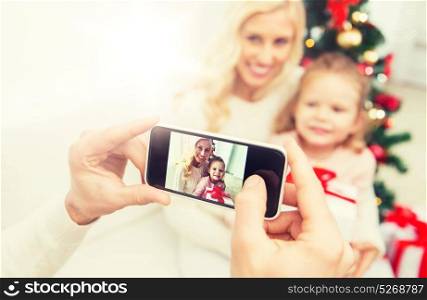 family, christmas, technology and people concept - close up of man taking picture of his family by smatrphone. man taking picture of his family by smatrphone