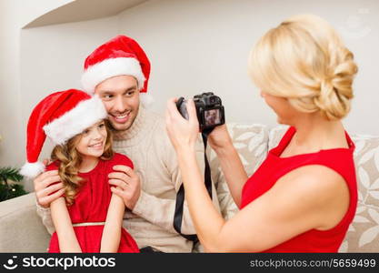 family, christmas, x-mas, happiness and people concept - mother taking picture of smiling father and daughter in santa helper hats