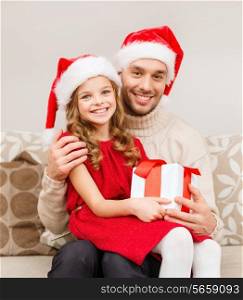 family, christmas, x-mas, happiness and people concept - smiling father and daughter in santa helper hats holding gift box