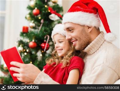 family, christmas, x-mas, happiness and people concept - smiling father and daughter in santa helper hats reading book