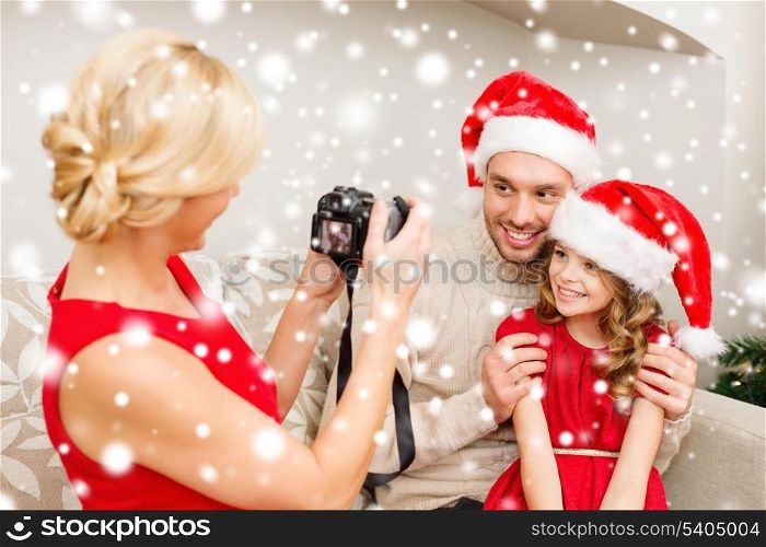 family, christmas, x-mas, winter, happiness and people concept - mother taking picture of smiling father and daughter in santa helper hats