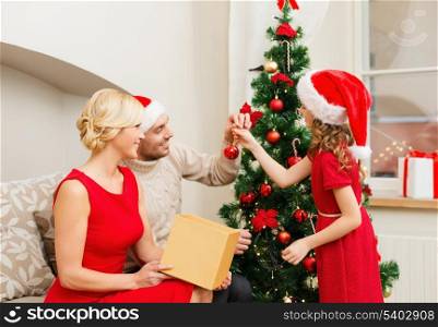 family, christmas, x-mas, winter, happiness and people concept - smiling family in santa helper hats decorating christmas tree