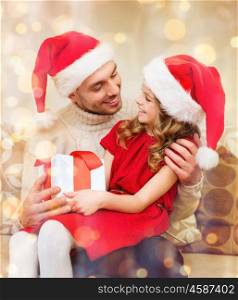 family, christmas, x-mas, winter, happiness and people concept - smiling father and daughter in santa helper hats holding gift box