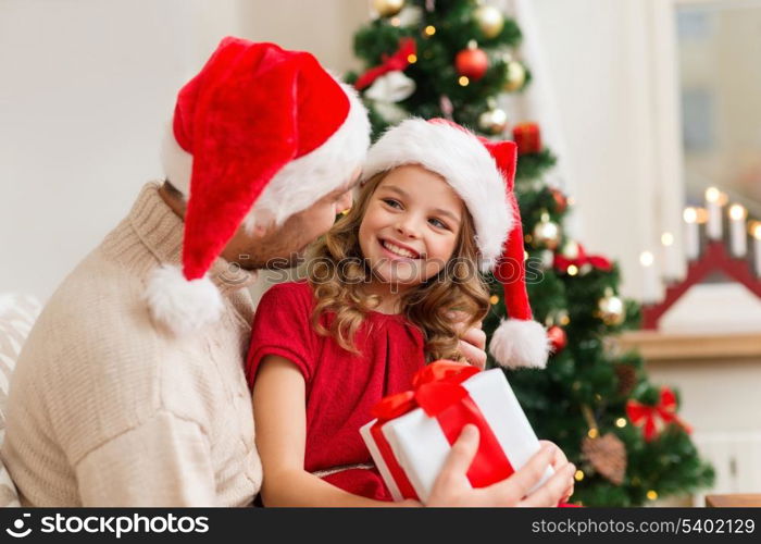 family, christmas, x-mas, winter, happiness and people concept - smiling father and daughter in santa helper hats holding gift box