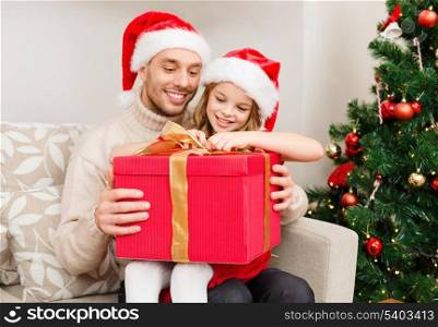 family, christmas, x-mas, winter, happiness and people concept - smiling father and daughter in santa helper hats opening gift box