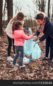 Family cleaning up a forest. Volunteers picking plastic waste to bags. Concept of plastic pollution and too many plastic waste. Environmental issue. Environmental damage. Responsibilitiy for environment. Real people, authentic situations