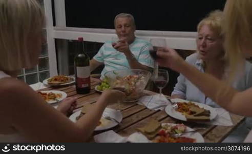 Family clinking glasses and smiling at dinner table in the evening.