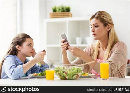 family, communication and people concept - sad girl looking at her mother with smartphone having dinner at home. sad girl looking at her mother with smartphone