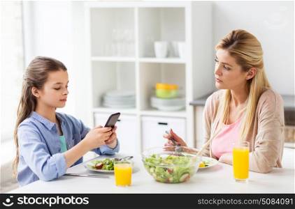 family, communication and people concept - sad mother looking at her daughter with smartphone having dinner at home. sad woman looking at her daughter with smartphone. sad woman looking at her daughter with smartphone