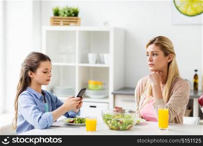family, communication and people concept - sad mother looking at her daughter with smartphone having dinner at home. sad woman looking at her daughter with smartphone