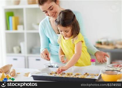 family, cooking and baking concept - happy mother and little daughter with chocolate sprinkles decorating cookies on tray at home kitchen. happy mother and daughter making cookies at home