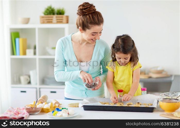 family, cooking and baking concept - happy mother and little daughter with chocolate sprinkles decorating cookies on tray at home kitchen. happy mother and daughter making cookies at home