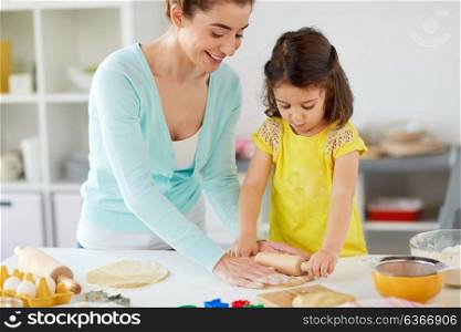 family, cooking and people concept - happy mother and little daughter with rolling pin making cookies from dough at home kitchen. happy mother and daughter making cookies at home