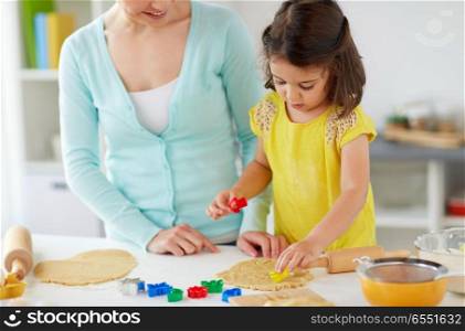 family, cooking and people concept - happy mother and little daughter with molds making cookies from dough at home kitchen. happy mother and daughter making cookies at home. happy mother and daughter making cookies at home