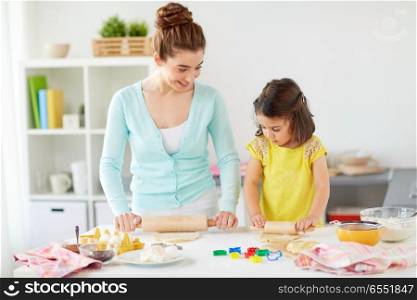 family, cooking and people concept - happy mother and little daughter with rolling pins making cookies from dough at home kitchen. happy mother and daughter making cookies at home. happy mother and daughter making cookies at home