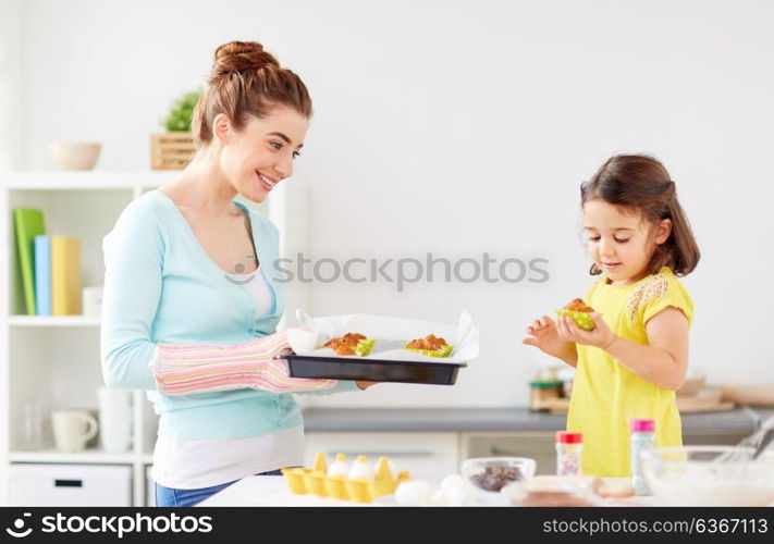 family, cooking and people concept - mother and little daughter baking muffins at home kitchen. mother and daughter baking muffins at home