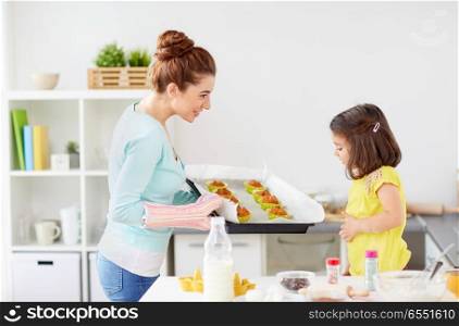 family, cooking and people concept - mother and little daughter baking muffins at home kitchen. mother and daughter baking muffins at home. mother and daughter baking muffins at home