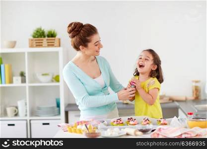 family, cooking and people concept - mother and little daughter making and decorating cupcakes with sprinkles at home kitchen. mother and daughter cooking cupcakes at home