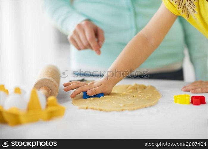 family, cooking and people concept - mother and little daughter with molds making cookies from dough at home kitchen. mother and daughter making cookies at home