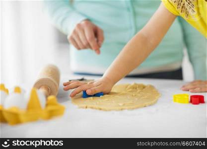 family, cooking and people concept - mother and little daughter with molds making cookies from dough at home kitchen. mother and daughter making cookies at home